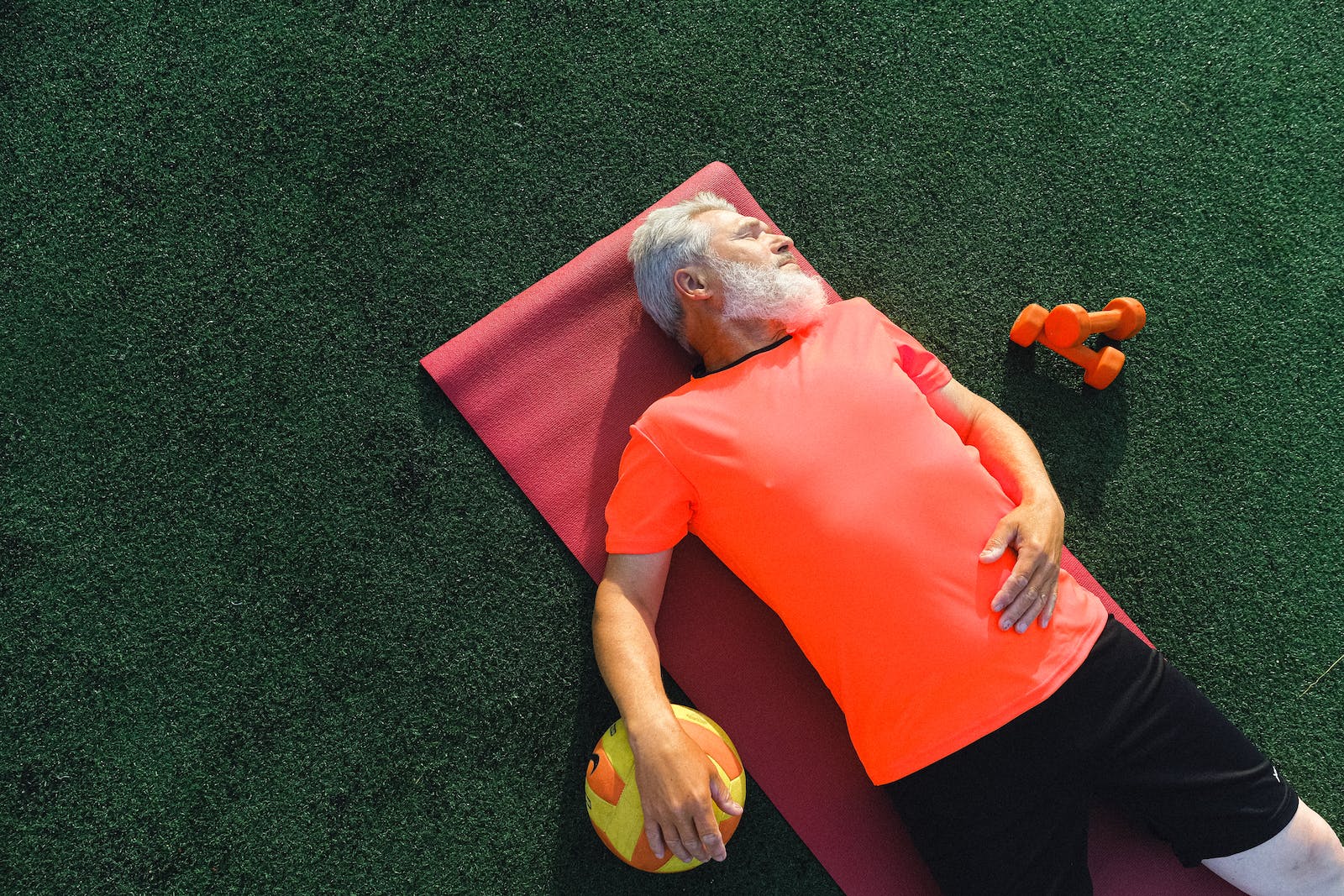 From above of tired senior sportsman lying on fitness mat near ball and dumbbells and resting after training in sunny day Fitness Equipment Recommendations for Seniors