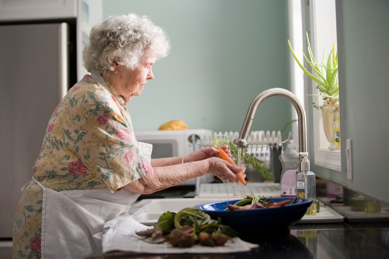 woman wearing yellow and pink floral dress wahing carrots Stay Active as a Senior